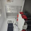 A photograph of meeting room 2. There is a white table with 5 red chairs and 1 white chair around it pushed up against the wall. A TV screen is on the wall above the table. There is a glass panel on the far wall looking into the corridor. 