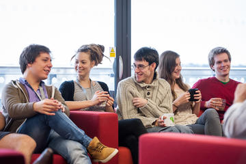 Photograph of a group of researchers sat on red sofas in the common room laughing and talking.